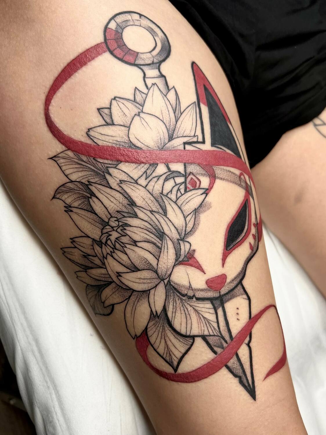 Татуировка маски и цветов на бедре с красными акцентами