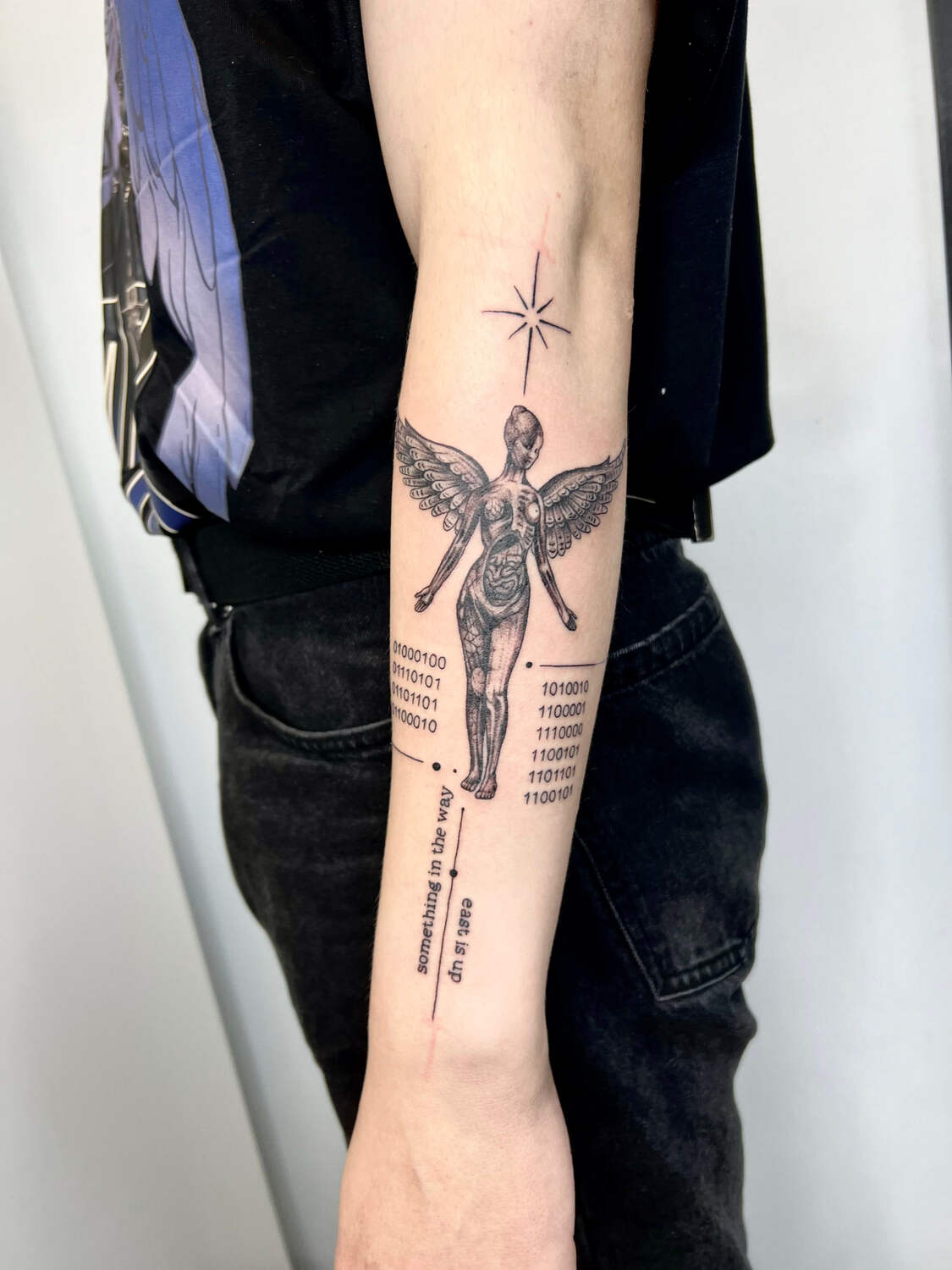 Татуировка на предплечье с фигурой ангела, бинарным кодом и минималистичной звездой