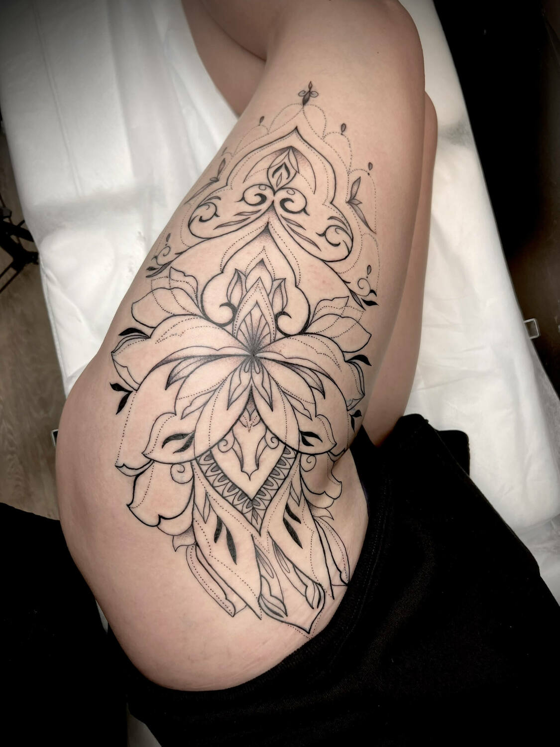 Орнаментальная татуировка на бедре с цветочными и геометрическими элементами