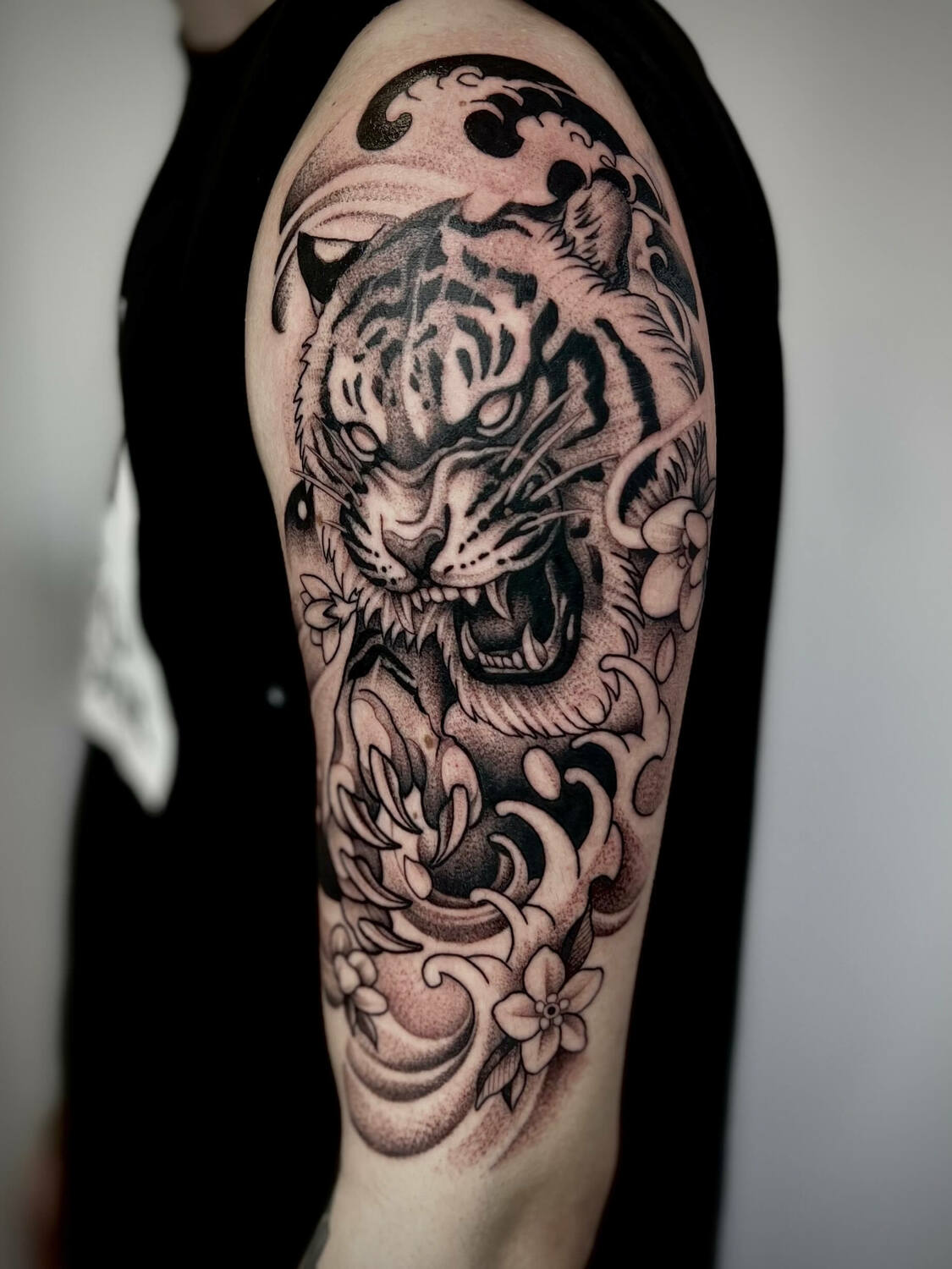 Татуировка тигра на плече в черно-белом стиле с волнами и цветами